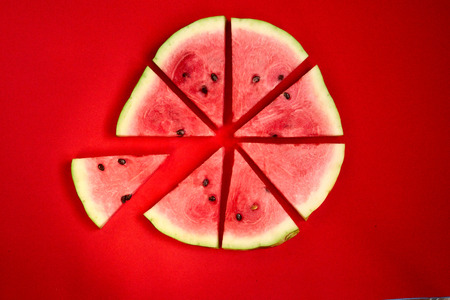 a circle of sliced triangles of watermelon on a red solid background , the concept of minimalismの写真素材