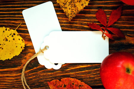 white labels, sheets of paper with red apples with yellow and red autumn leaves on wooden brushed...