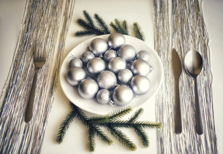 Picture of Christmastime table setting, white festive plate with knife and fork, shiny silver...