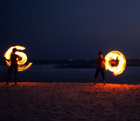 High Skill Man playing fireworks by spinning wood pole with fuel oil and fire, circle around as ring of fire on beach along ocean in tropical island, long high exposure blur movement.の写真素材