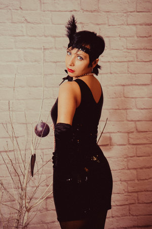 a girl with short black hair with a bandage with sequins and feathers on her head in a dress with...