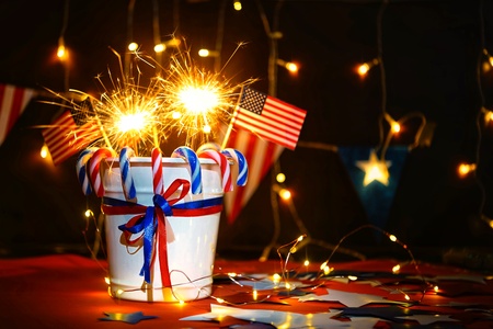 Fireworks display celebrates the independence Day of the United States of America nation on the fourth of July with the us flag , sparklers , candy, on the red background and on the background of Christmas garland and bokeh, with the stars , the end of the Celebration of freedom.の写真素材