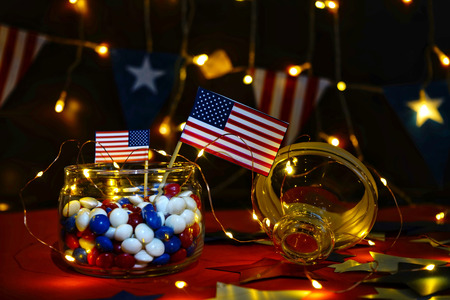 Fireworks display celebrates the independence Day of the United States of America nation on the fourth of July with the us flag , sparklers , candy, on the red background and on the background of Christmas garland and bokeh, with the stars , the end of the Celebration of freedom.の写真素材