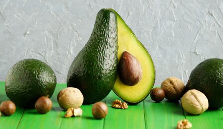 Avocado cut in half stands on a green wooden table surrounded by nut, snack Keto diet.の写真素材