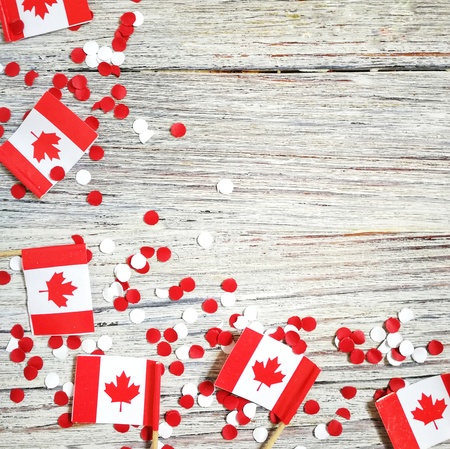The national holiday of July 1- happy Canada day , Dominion day, the concept of patriotism, independence and memory, a place for text. white red confetti and mini flags on a wooden tableの写真素材