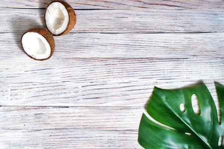 two halves and one whole coconut with a leaf of tropical monstera plant on a white wooden background. Flat layer, top view, copy space. Summer background, nature. Healthy cooking. Creative concept of healthy eating. horizontal photoの写真素材