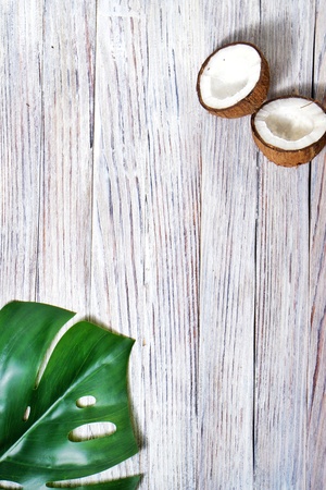 two halves and one whole coconut with a leaf of tropical monstera plant on a white wooden background. Flat layer, top view, copy space. Summer background, nature. Healthy cooking. Creative concept of healthy eating. horizontal photoの写真素材