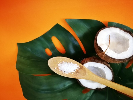 coconuts and leaf of tropical monstera plant with coconut flakes on orange background. Flat layer, top view, copy space. Healthy cooking. Creative concept of healthy food and ecology.の写真素材