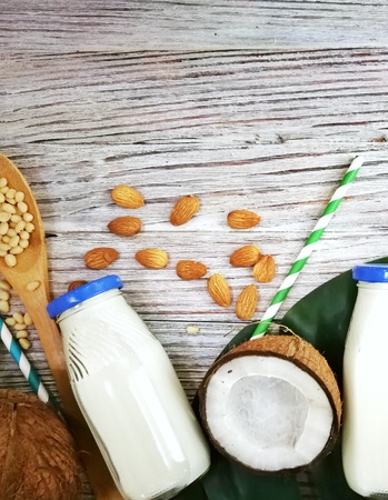 coconuts, tropical monstera plant leaf and vegan milk in bottle on white wooden background. Flat layer, top view, copy space. Healthy cooking. Creative concept of healthy food and ecology.の写真素材
