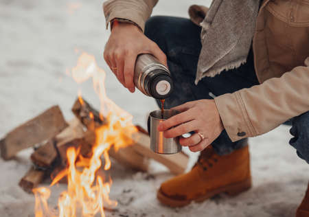 A man in the winter forest by the fire pours coffee. high quality photoの写真素材