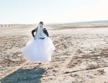 Blonde girl in a wedding dress and a leather jacket in a rock style on a wild sandy beach. high quality photoの写真素材