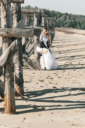 Blonde girl in a wedding dress and a leather jacket in a rock style on a wild sandy beach. high quality photoの写真素材