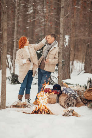 A couple in love, a man and a woman in a winter forest around a campfire drink coffee and give marshmallows. high quality photoの写真素材