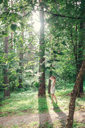 Blonde girl in a light airy dress, barefoot at dawn in a summer forest. high quality photoの写真素材