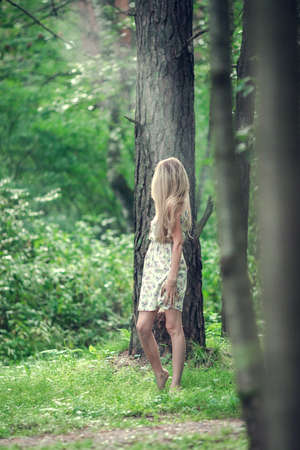 Blonde girl in a light airy dress, barefoot at dawn in a summer forest. high quality photoの写真素材