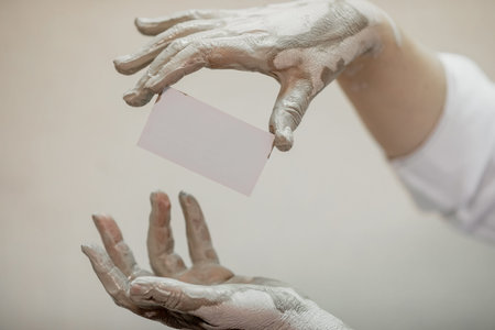 Hands in clay after work at the potters wheel, close-up holding a mockup of a business cardの写真素材