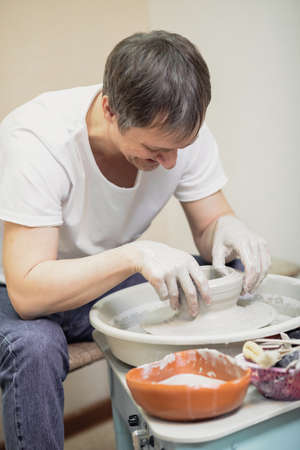 A man in a white T-shirt and jeans , in a pottery workshop, working behind a potter's wheel. high quality photoの写真素材