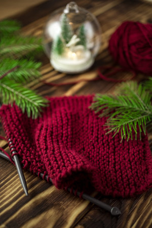 Started knitting on knitting needles, with yarn on a rustic wooden table, with green branches of a...