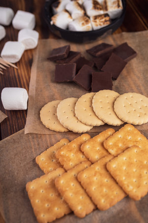 marshmallows, chocolate and cookies for making smore on brown background. view from above. copy...