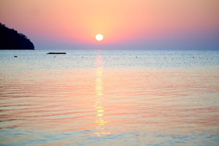 Orange sunset above sea with boat amazing Golden reflection of the sun on the calm wavesの写真素材