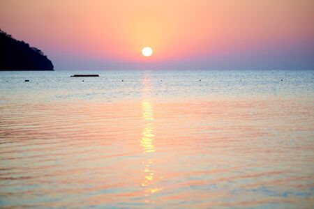 Orange sunset above sea with boat amazing Golden reflection of the sun on the calm wavesの写真素材