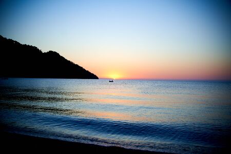 Orange sunset above sea with boat amazing Golden reflection of the sun on the calm wavesの写真素材