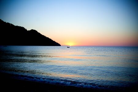 Orange sunset above sea with boat amazing Golden reflection of the sun on the calm wavesの写真素材