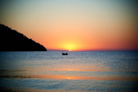 Orange sunset above sea with boat amazing Golden reflection of the sun on the calm wavesの写真素材