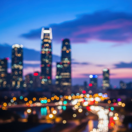 A soft focus view of a city skyline at twilight, featuring tall buildings with glowing windows and blurred streetlights creating bokeh effects.の素材