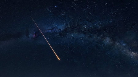 A vivid image of a shooting star streaking across the night sky, with the Milky Way galaxy serving as a stunning backdrop. The star trail is captured in a bright, elongated path, highlighting the beauty and vastness of the cosmos. The deep blue and black hues of the sky contrast with the luminous trail, creating a mesmerizing celestial scene.の素材