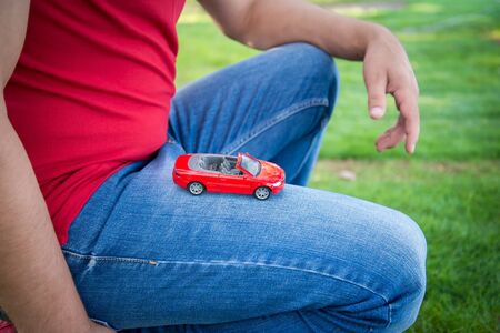 red toy car on the knee the man in the red shirt and blue jeans on the green grassの写真素材