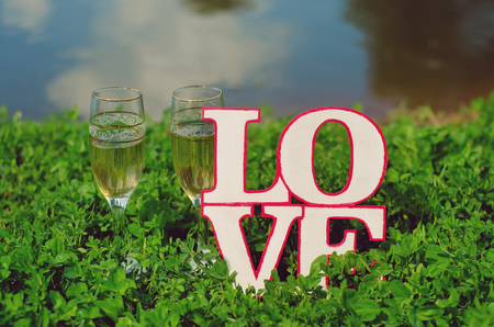 Glasses with champagne and homemade wooden plaque with the word love in the grass are beautifulの写真素材