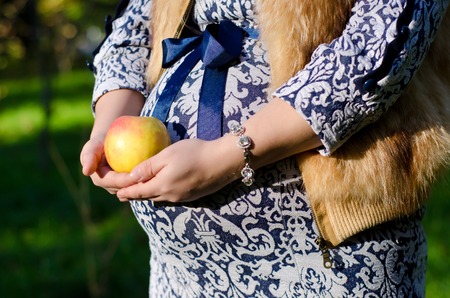 pregnant woman in blue dress holds a round yellow appleの写真素材