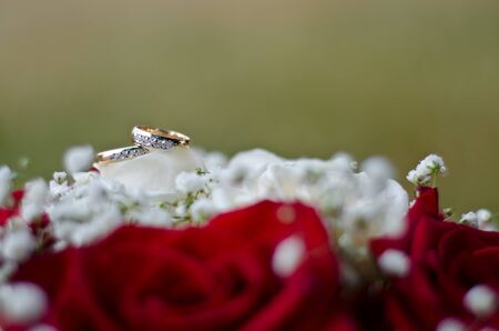Gold wedding rings on a bouquet of white and red flowers on a background of green grassの写真素材