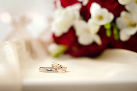 Beautiful wedding rings on a white background with a white and red bouquetの写真素材