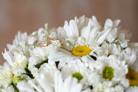 Gold wedding rings lie on a bouquet of white daisiesの写真素材