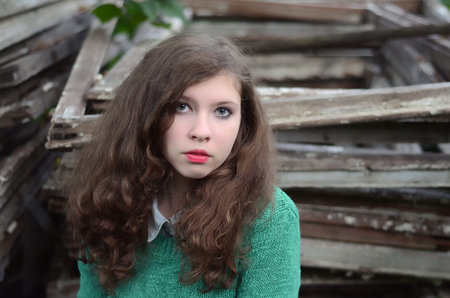 Young girl with long brown hair and blue eyes wearing a green sweater, in the garden in the summer