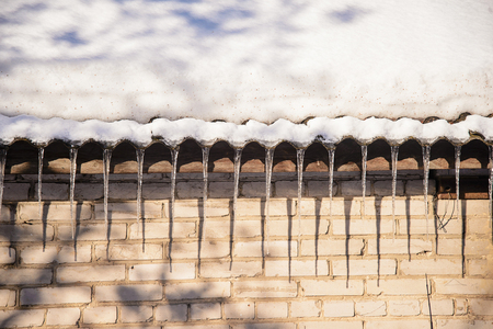 Spring icicles hanging from the roof of the old brick houses with snow-covered roofの写真素材