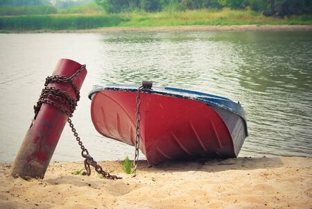 Old red boat chained to a peg on the sandy shoreの写真素材