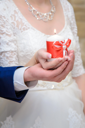 The bride and groom hold a festive candle in hand togetherの写真素材