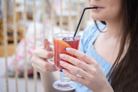 Girl in a blue blouse drinking mulled wine from a glass through a straw for a table in a cafeの写真素材