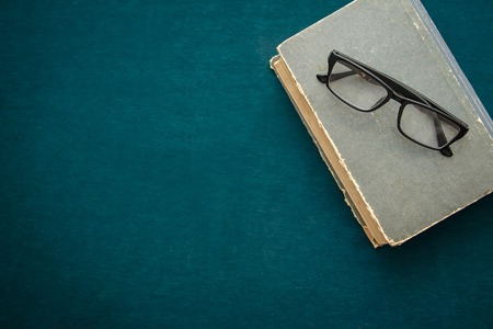 Black sunglasses lay on the old closed the book on a dark green backgroundの写真素材