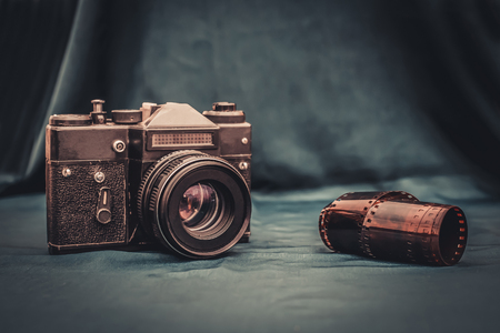 Old retro photo camera and rolled photographic film are on the table on the dark green background of the fabricの写真素材