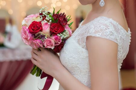 Wedding bouquet of red and pink roses with a red ribbon in the hands of the bride in a white closeupの写真素材