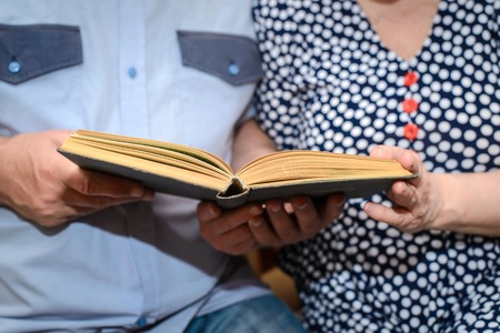 An elderly couple - grandfather in the blue shirt and the grandmother in the blue dress with white polka dots holding a book and reading it together closeupの写真素材