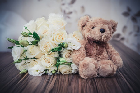 Wedding bouquet of white roses and a cute Teddy bear on the tableの写真素材