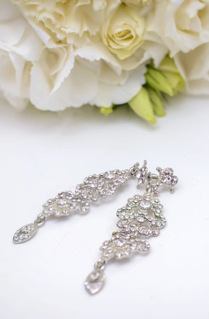 Beautiful wedding jewelry: earrings for bride near a bouquet on a white surface