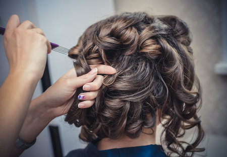The hands of the hairdresser do Bridal hairstyle with curls for long brown hair closeup