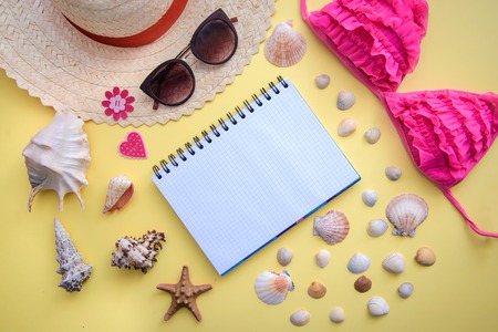 Holiday plans at sea: ?otepad, shells, sunglasses, a straw hat, a pink bathing suit on yellow background, top viewの写真素材