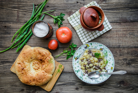 Simple food: pot with hot meat and potatoes, red ripe tomatoes, round appetizing flat cake, greens, salt on a wooden rustic backgroundの写真素材